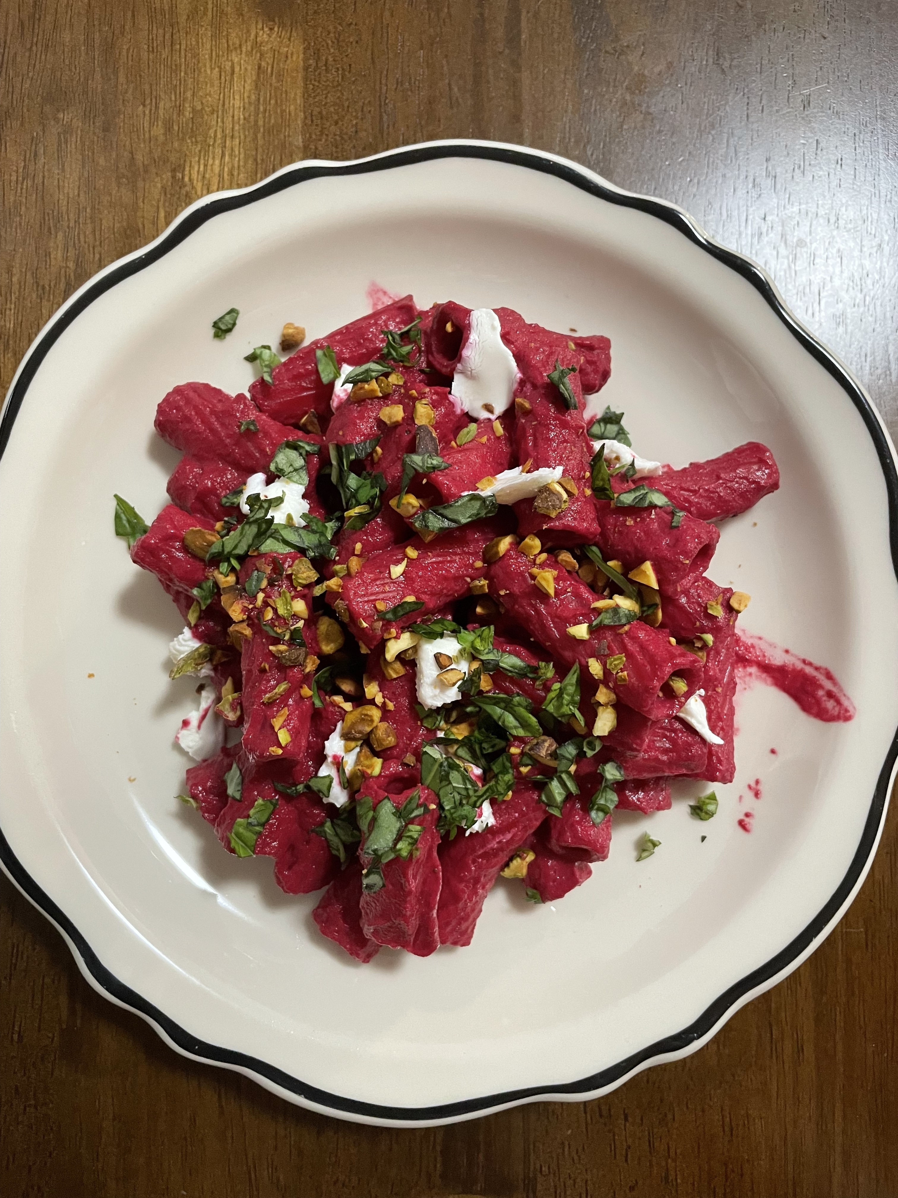A plate of beet pasta topped with herbs, nuts, and goat cheese