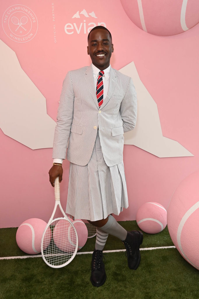 Ncuti in a unique striped suit with skirt bottom, holding a tennis racket, at a themed event