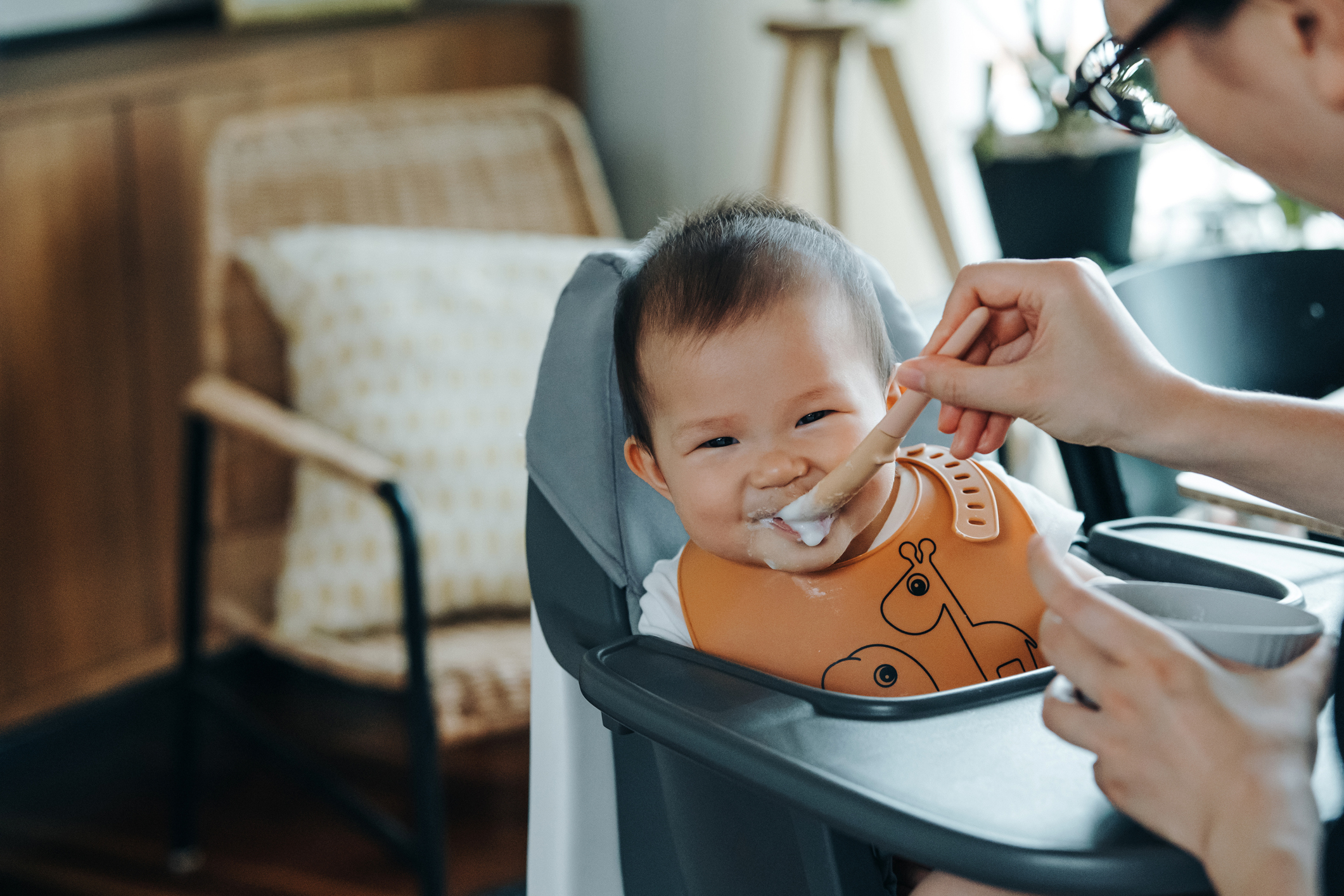 Baby being fed in a high chair, smiling with a bib on