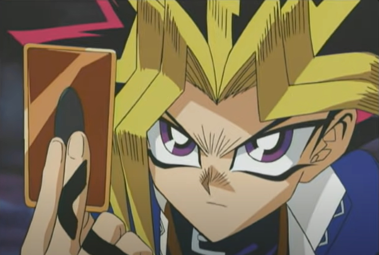 Yugi from Yu-Gi-Oh holds up a card with intense focus, wearing his signature blue jacket