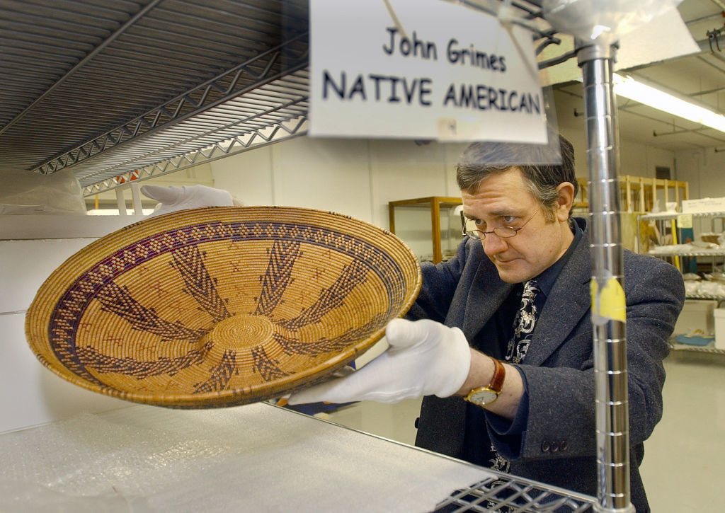 Person examining a Native American woven basket; sign reads &#x27;John Grimes NATIVE AMERICAN&#x27;