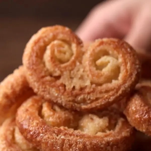 A person holds a palmier pastry, with more pastries stacked beneath it