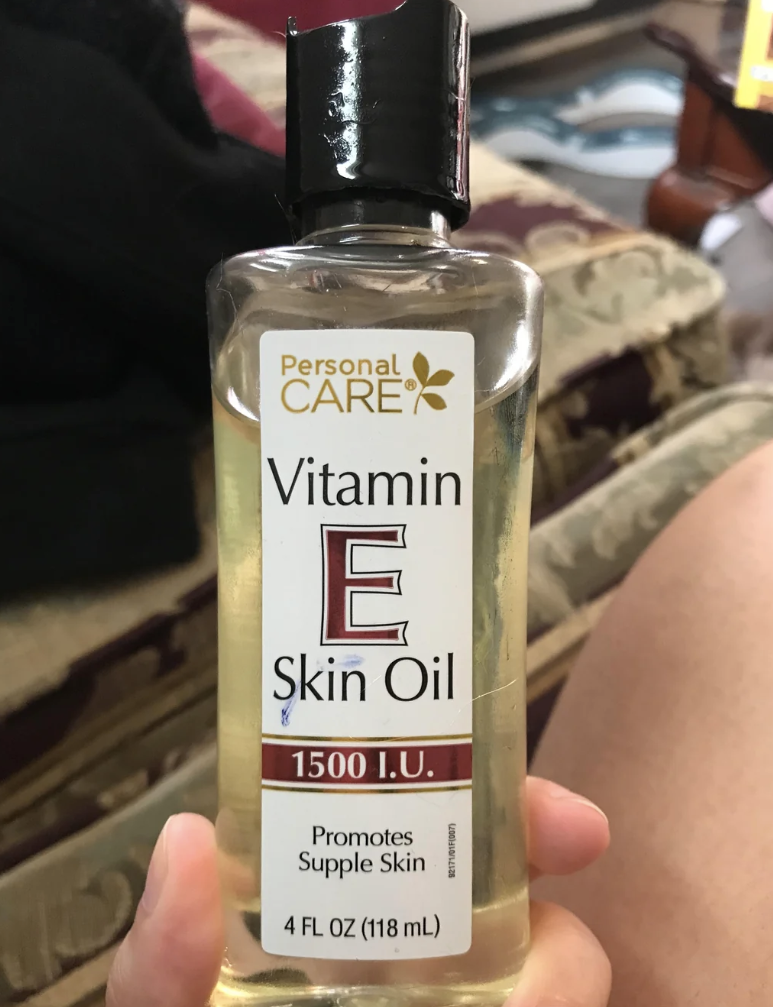Person holding a bottle of vitamin E skin oil with a detailed label, resting on their lap.
