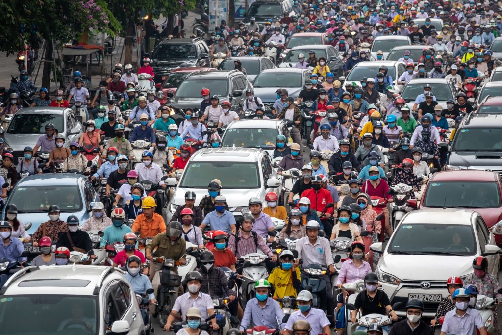 A congested street filled with cars and many motorcyclists wearing helmets