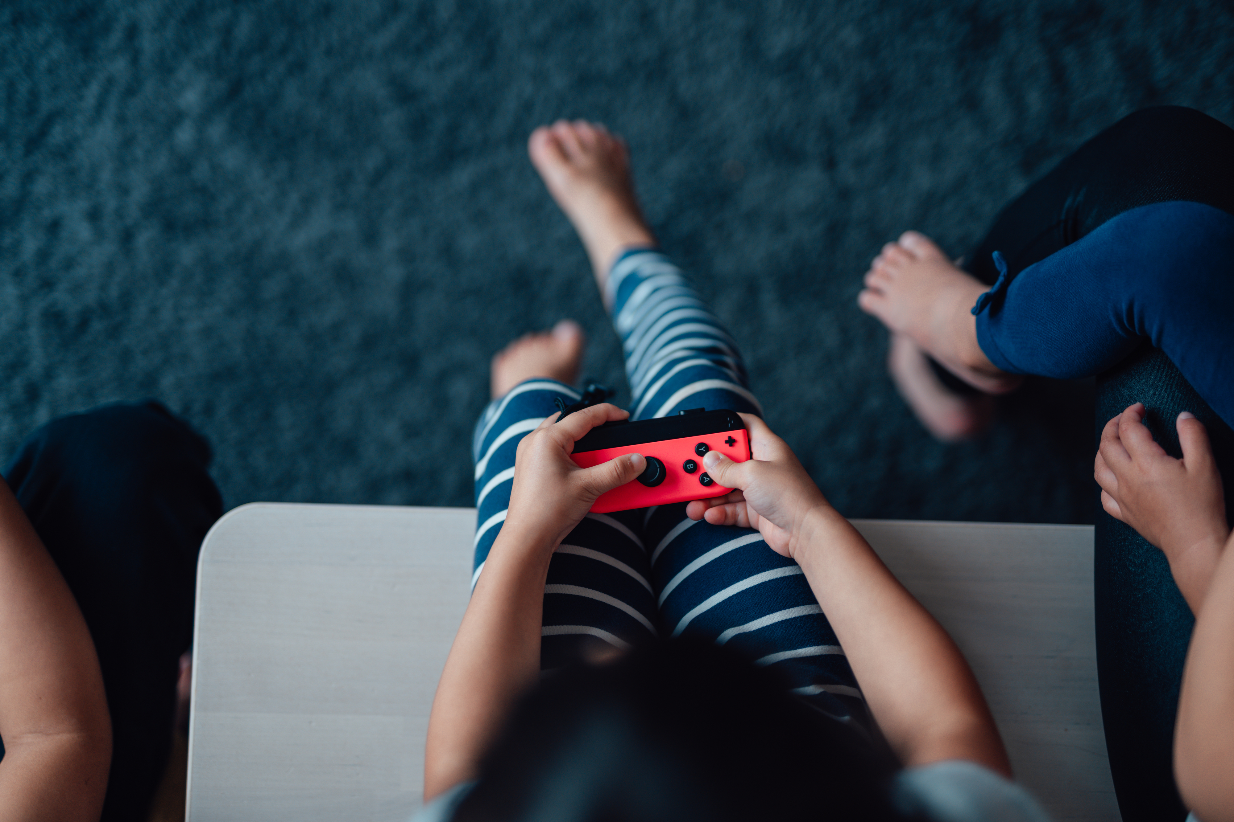Top view of a child holding a game controller with another person seated nearby, suggesting shared playtime or parental supervision