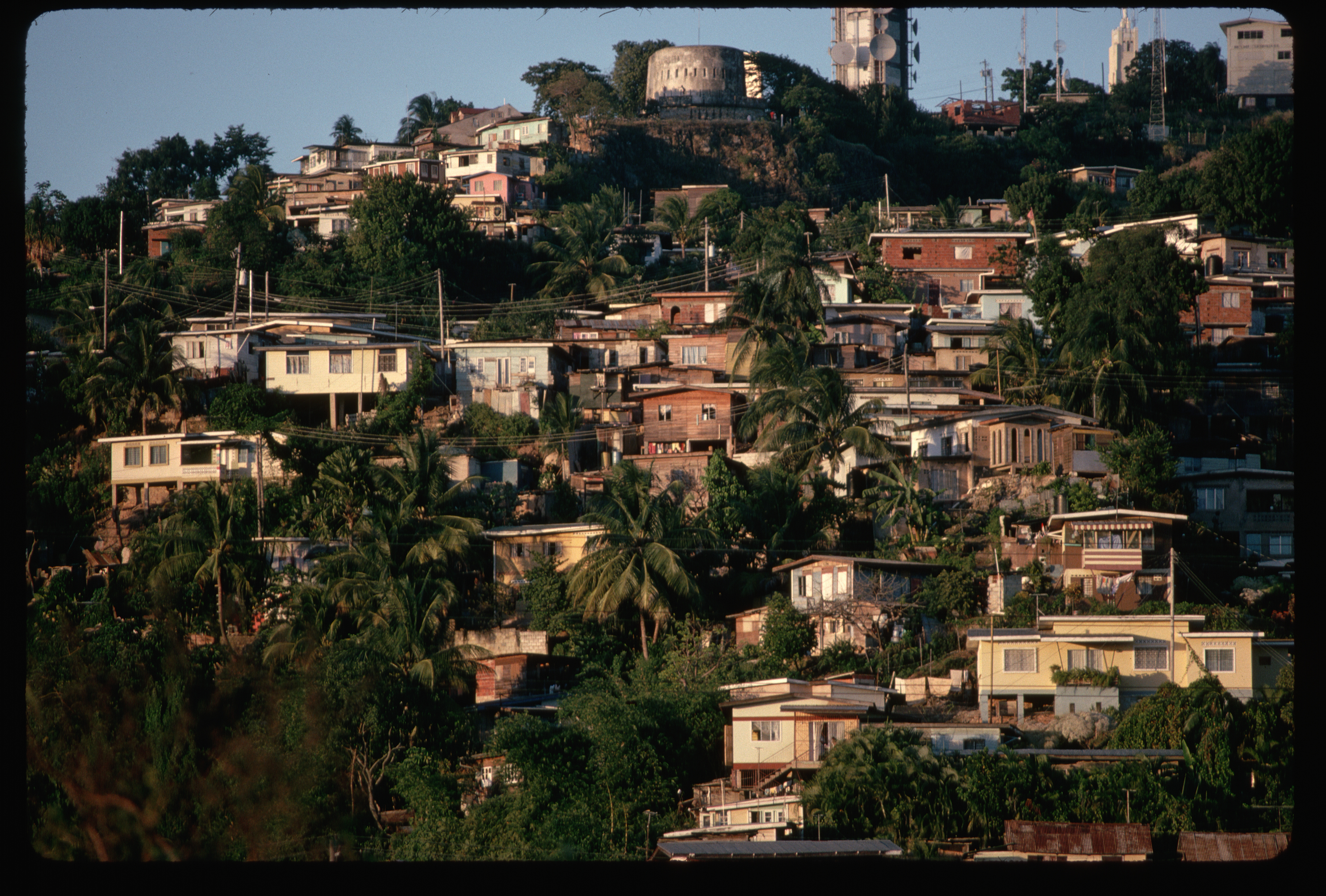 Hillside with dense cluster of houses and vegetation, with a large monument visible in the background