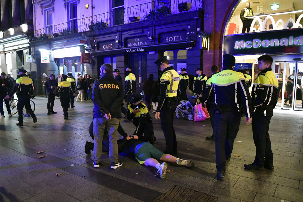 Garda officers responding to an incident on a city street at night with onlookers in the background