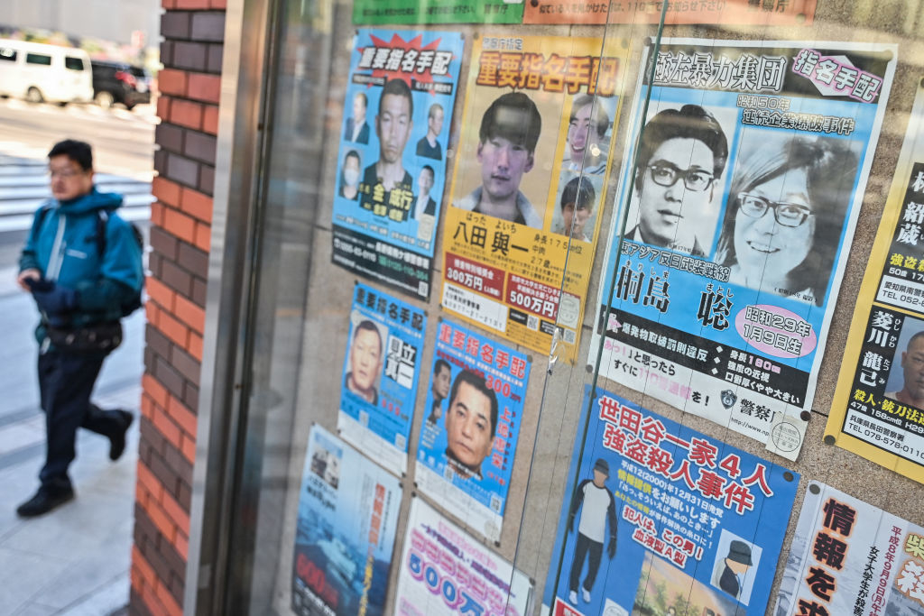 Person walking past a bulletin board with various flyers, some with images of individuals&#x27; faces. Text is mostly in Chinese