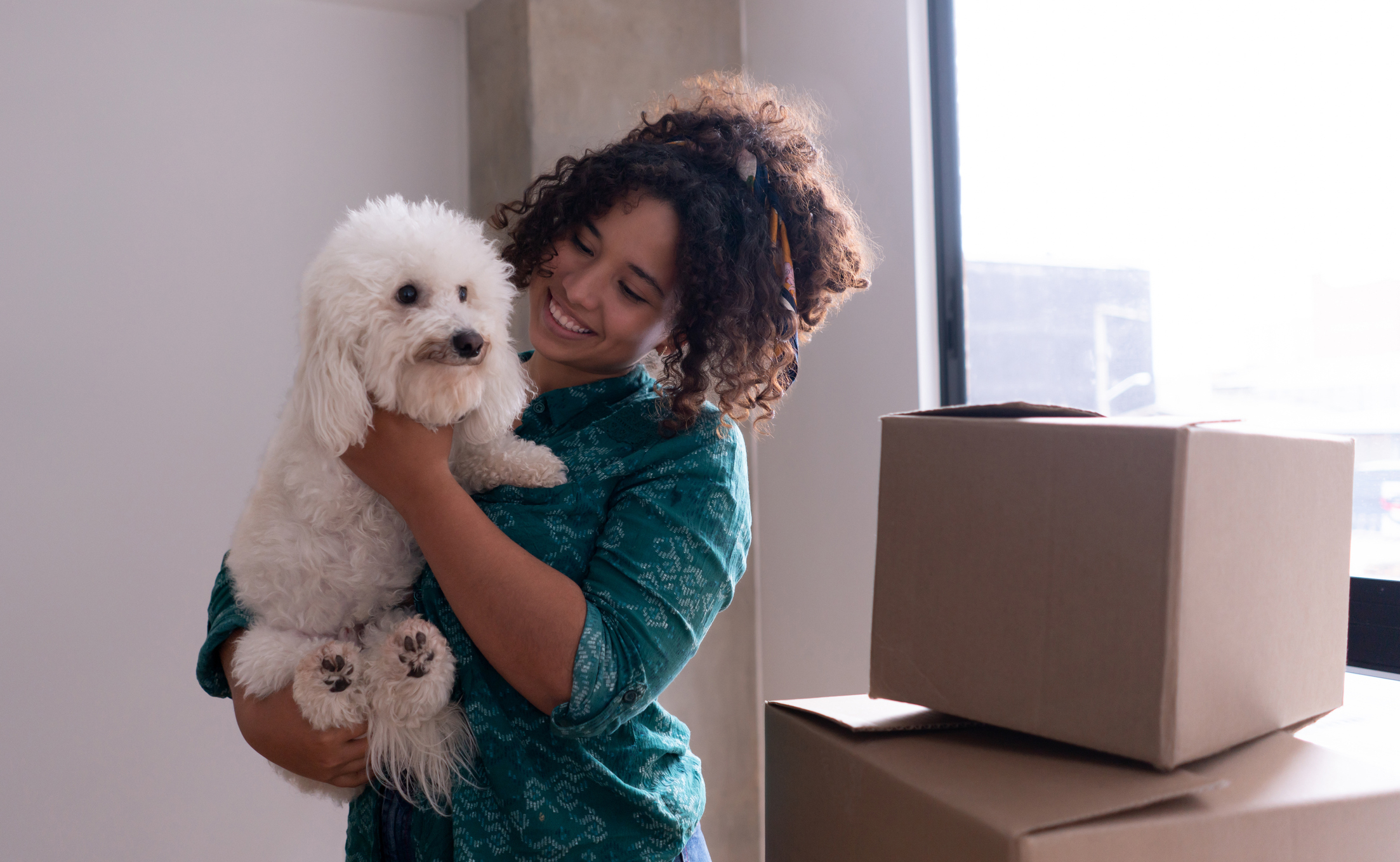 Woman embracing a dog with affection, standing near a cardboard packing box in a room