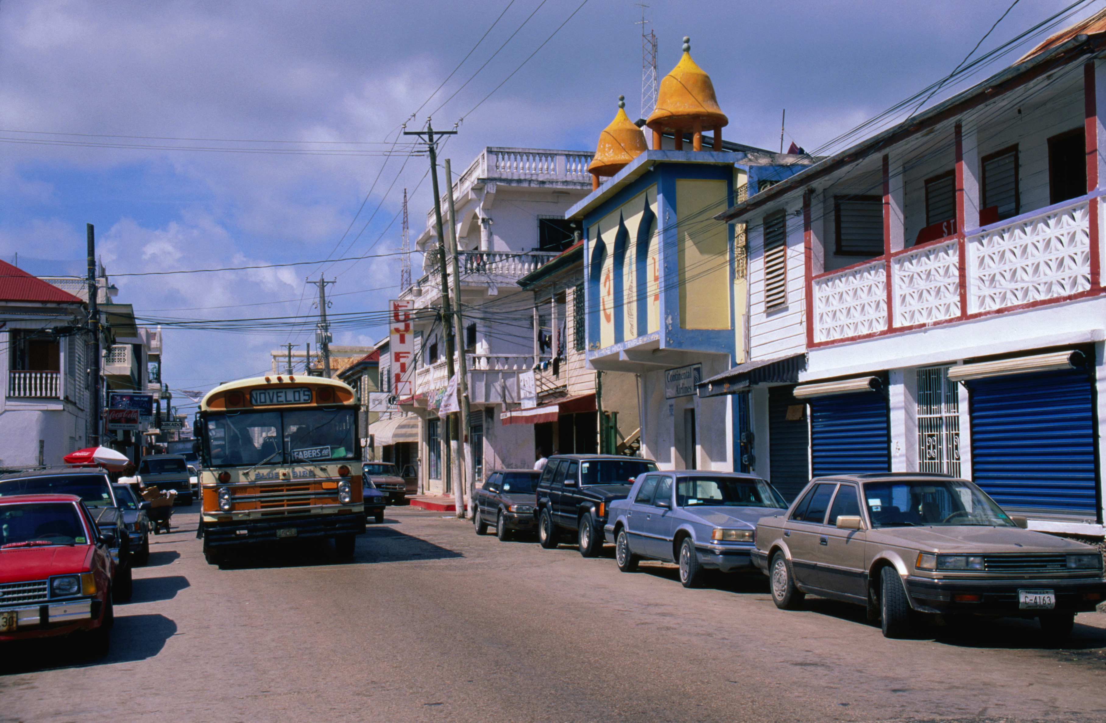 Street view with vehicles parked and a bus in motion, traditional buildings with decorative elements on facades, and a dome structure
