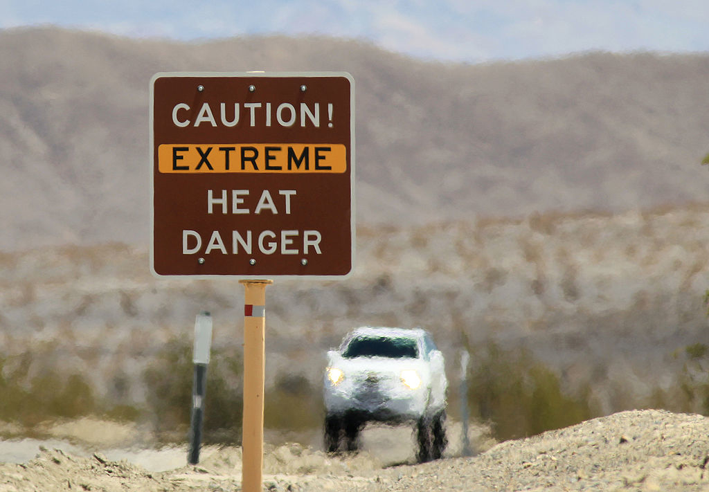 Warning sign for extreme heat danger with a blurry car in the background