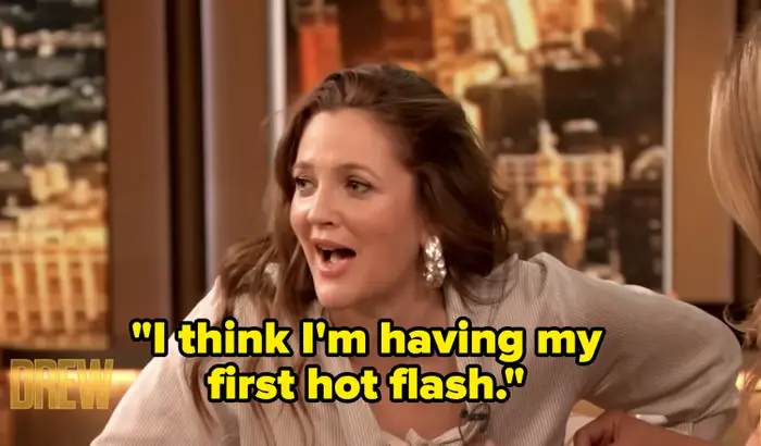 Drew Barrymore in a talk show setting with a surprised expression, captioned with her quote on experiencing a hot flash