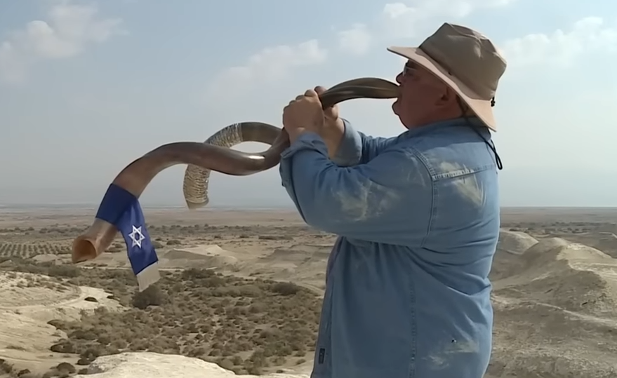 Man blowing a shofar in a desert landscape with an Israeli flag nearby; title reads &quot;Meet the &#x27;BEST Shofar Sounder&#x27; in the modern world&quot;