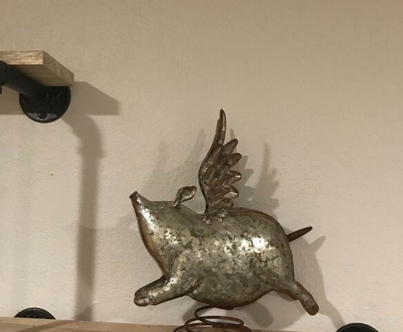 Metallic flying pig sculpture on a wall shelf