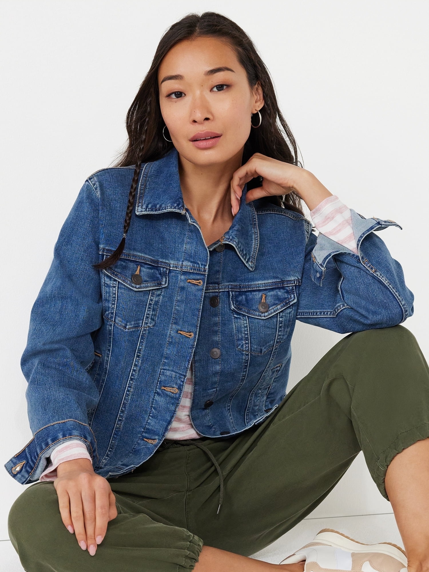 A model wearing a casual denim jacket, striped tee, olive green pants, and white sneakers