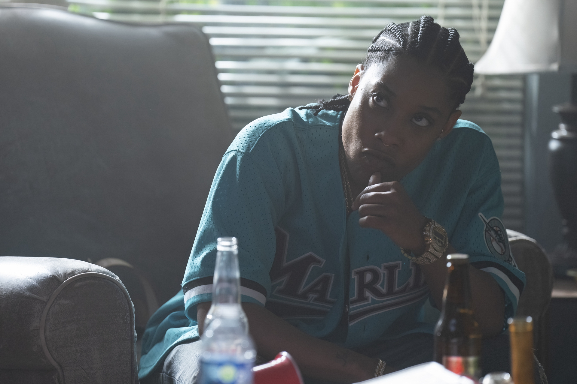 Chastity in a Marlins jersey leans on a couch, looking pensive, with beverages on the table