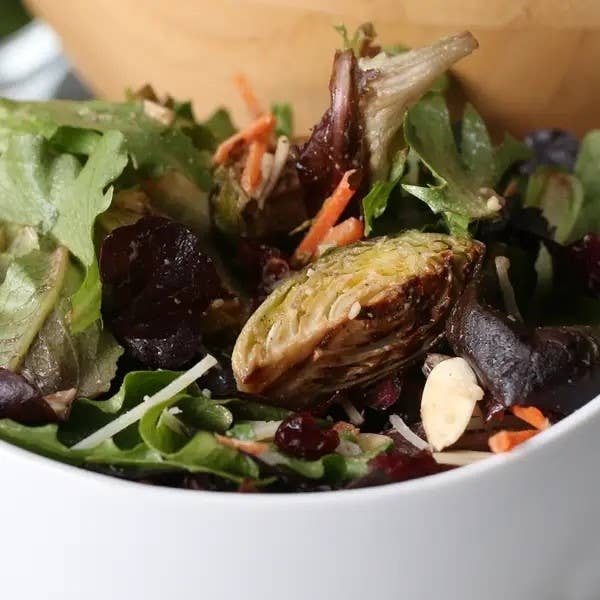 A close-up of a fresh mixed salad with various greens, mushrooms, and roasted Brussels sprouts in a bowl