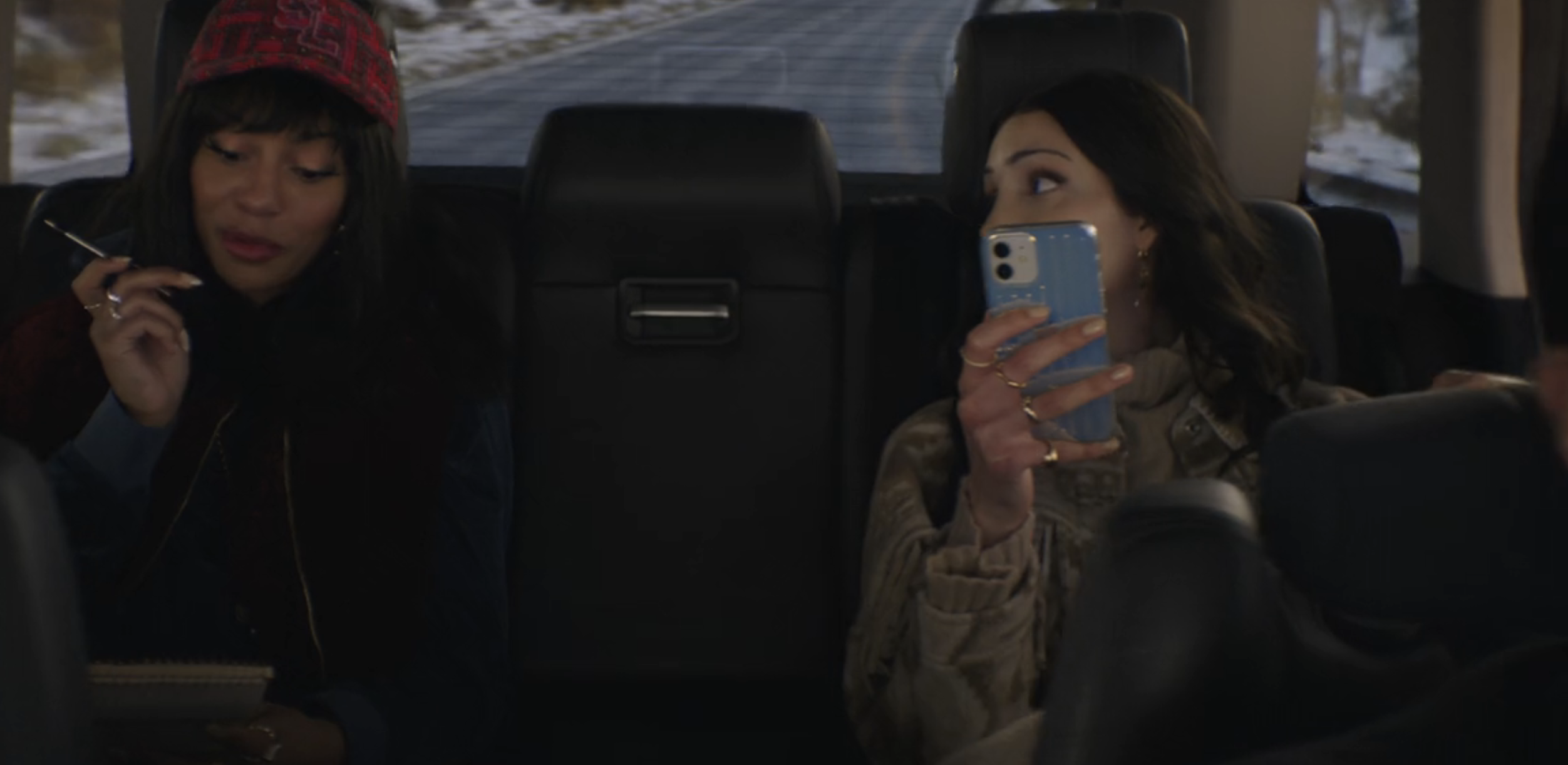 Two women in a car; one is eating as the other takes a selfie