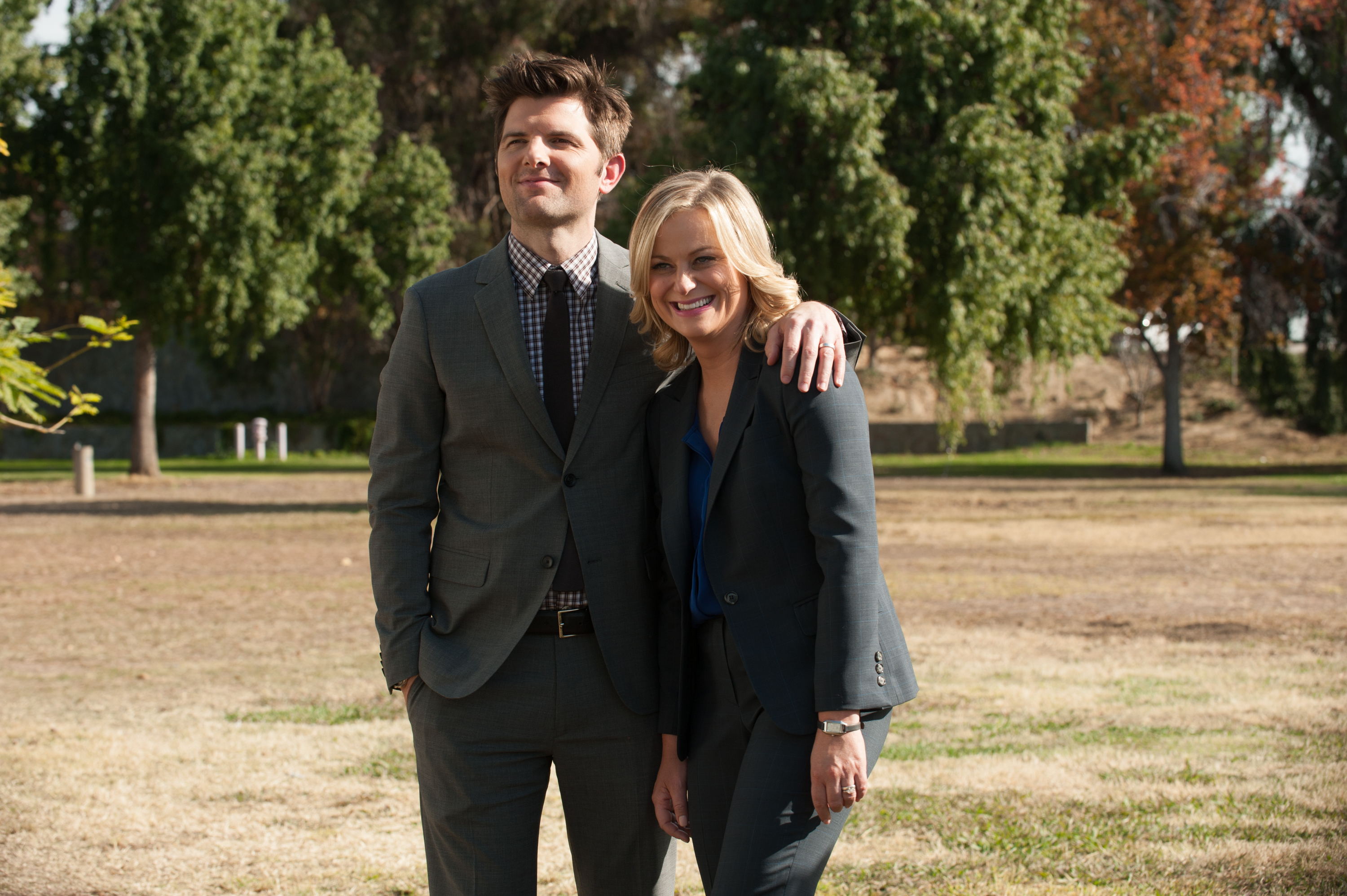 Leslie Knope and Ben Wyatt smiling together in business attire outdoors