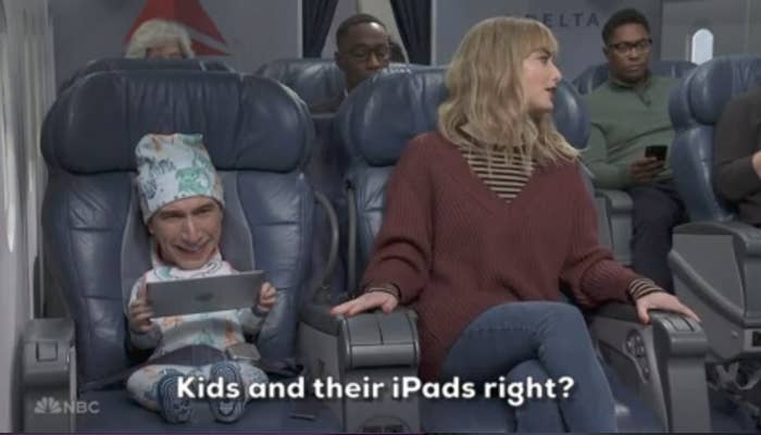 Two characters on an airplane; one, a baby with a human head, holding a tablet, both seated, with text &quot;Kids and their iPads right?&quot;