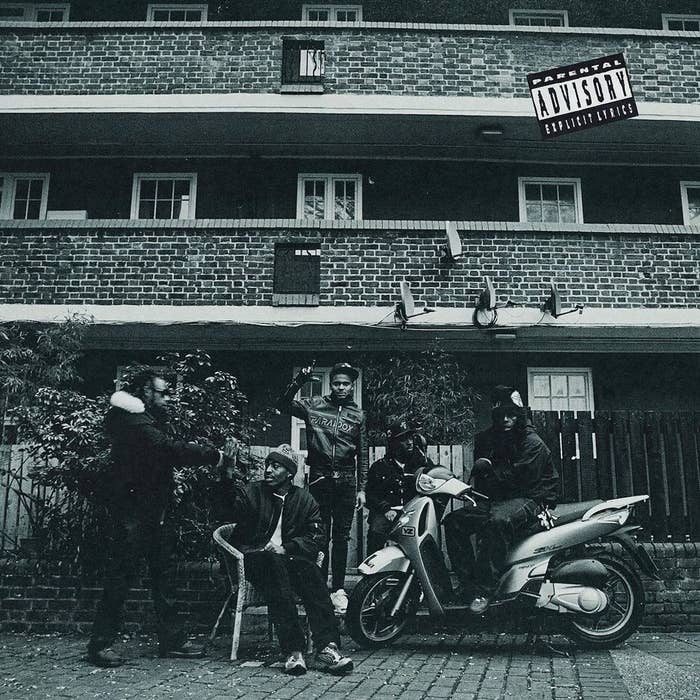 Group of people posing with a scooter in front of a building; includes a parental advisory label