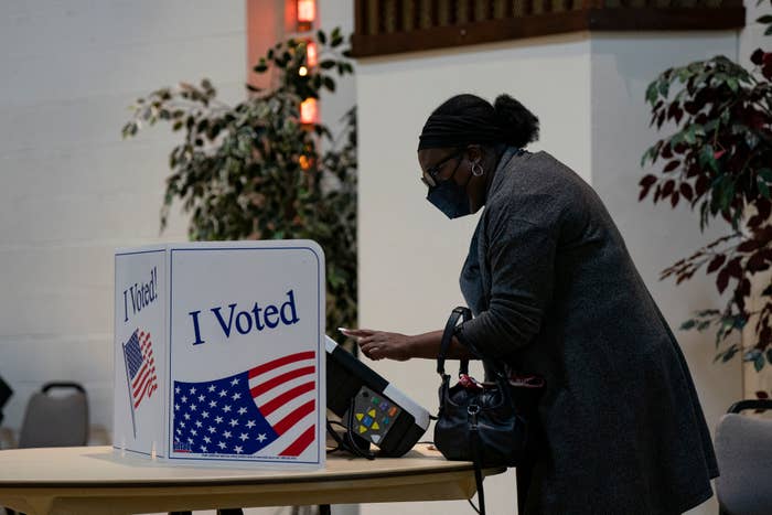 Person wearing a mask casting a ballot at an &quot;I Voted&quot; booth