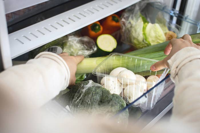 Person&#x27;s hands placing fresh vegetables into a fridge, suggesting tips for food storage