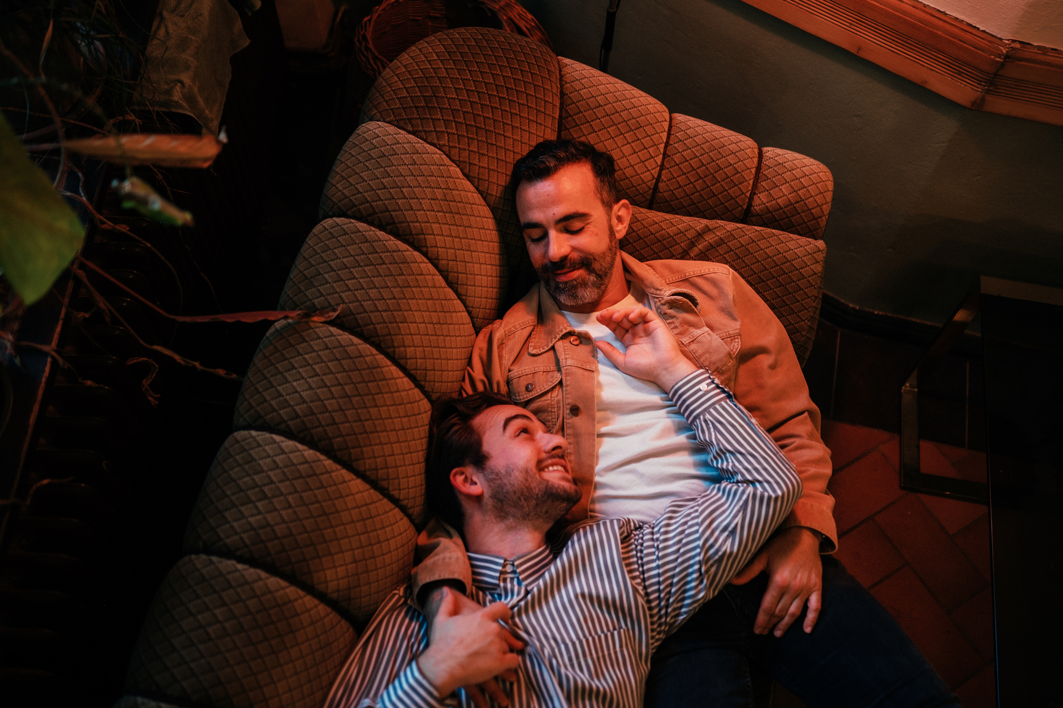 Two men lounging closely on a couch, sharing a moment of affectionate connection