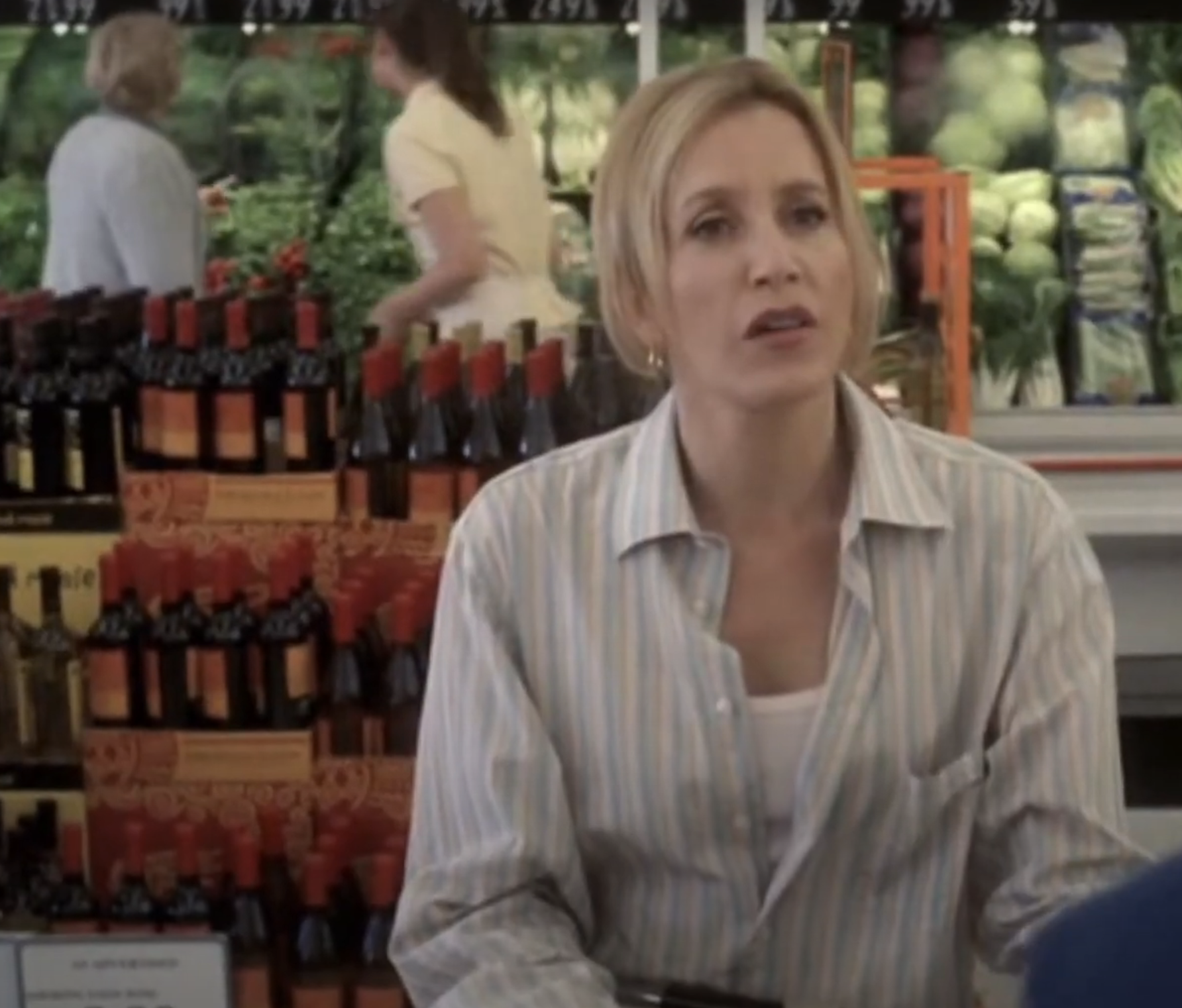 Woman in a striped shirt shopping at a grocery store with produce and wine shelves in the background