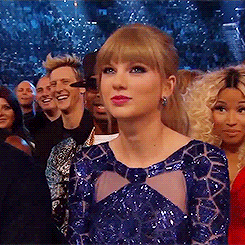 Taylor Swift in a blue dress with geometric patterns, sitting among an audience