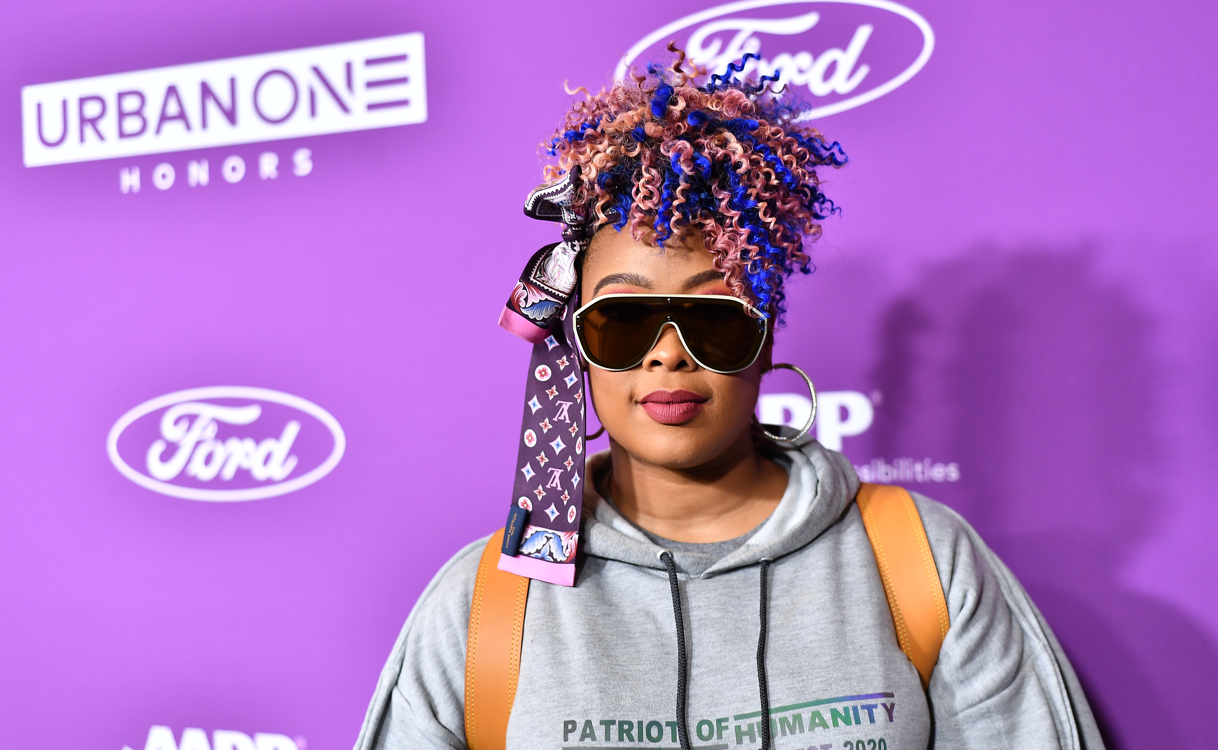 Da Brat at an event wearing a hooded outfit with ribboned braids and sunglasses