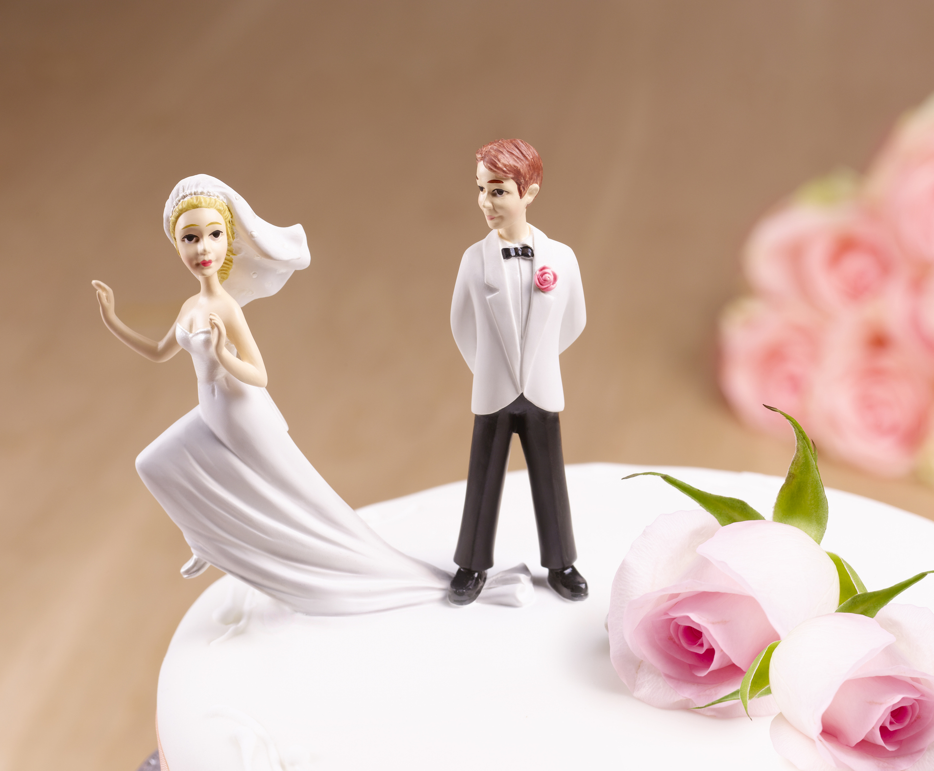 Bride and groom figurines on a wedding cake with pink roses