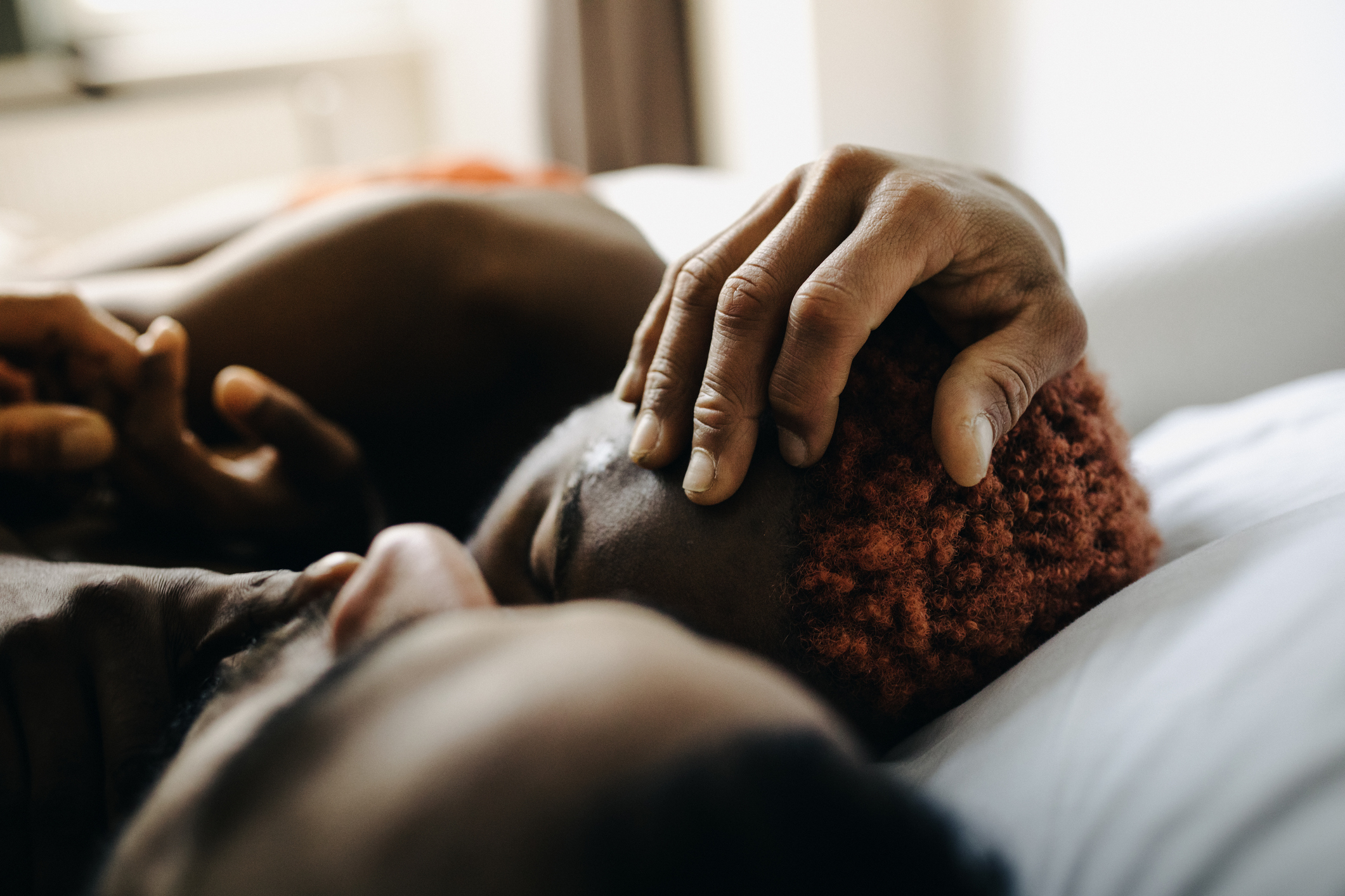 Two people embracing intimately on a bed, one caressing the other&#x27;s head