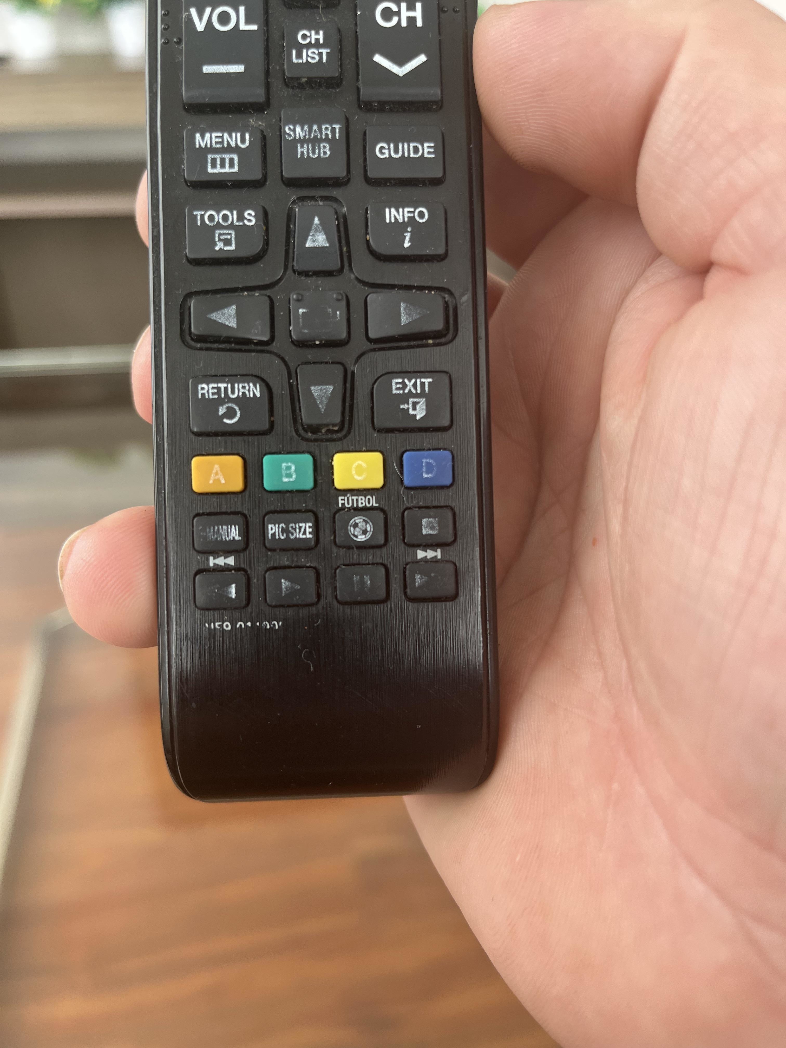 Person holding a television remote with various buttons for functions like volume, channel selection, and settings