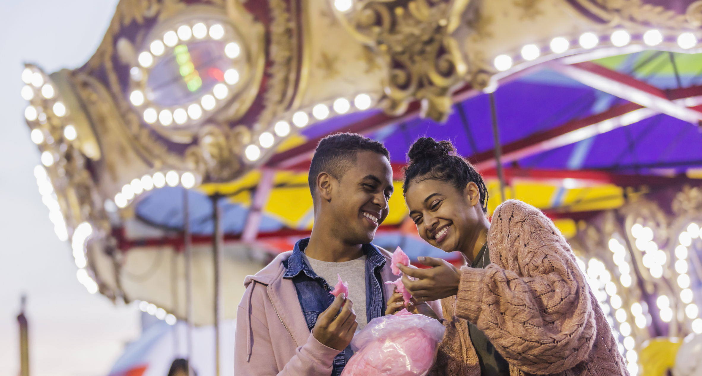 A couple sharing cotton candy and smiling at a carnival