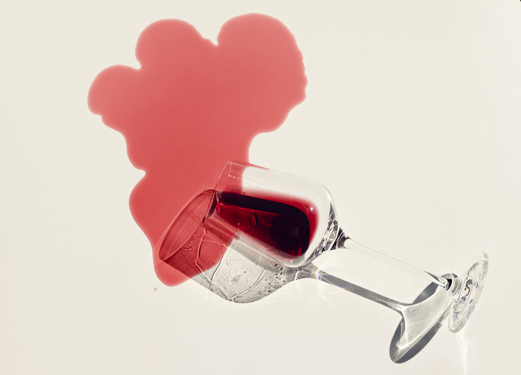 Wine glass tipped over with red liquid splashing out in the shape of a heart