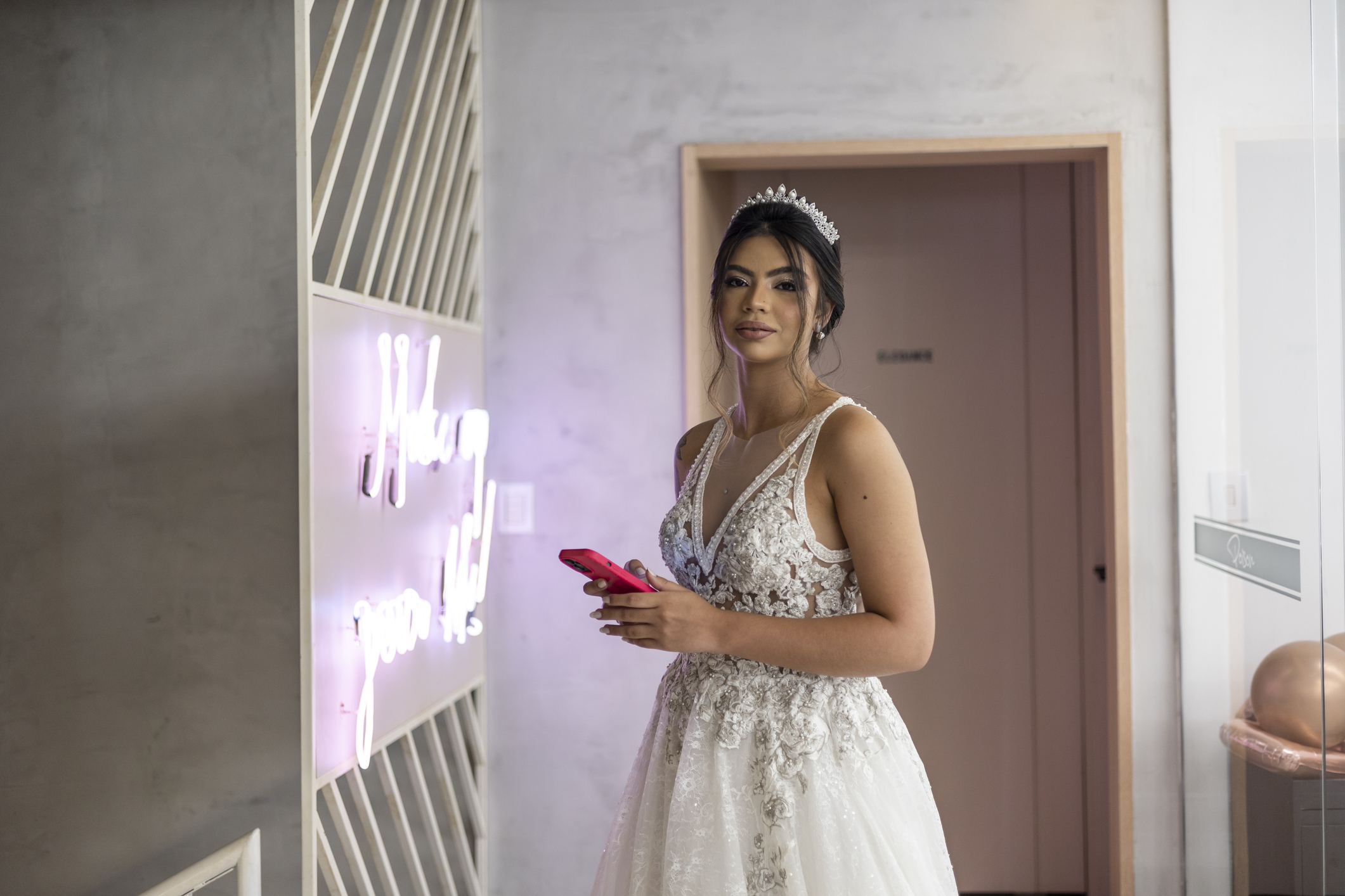 Woman in wedding dress holding phone, standing beside neon sign