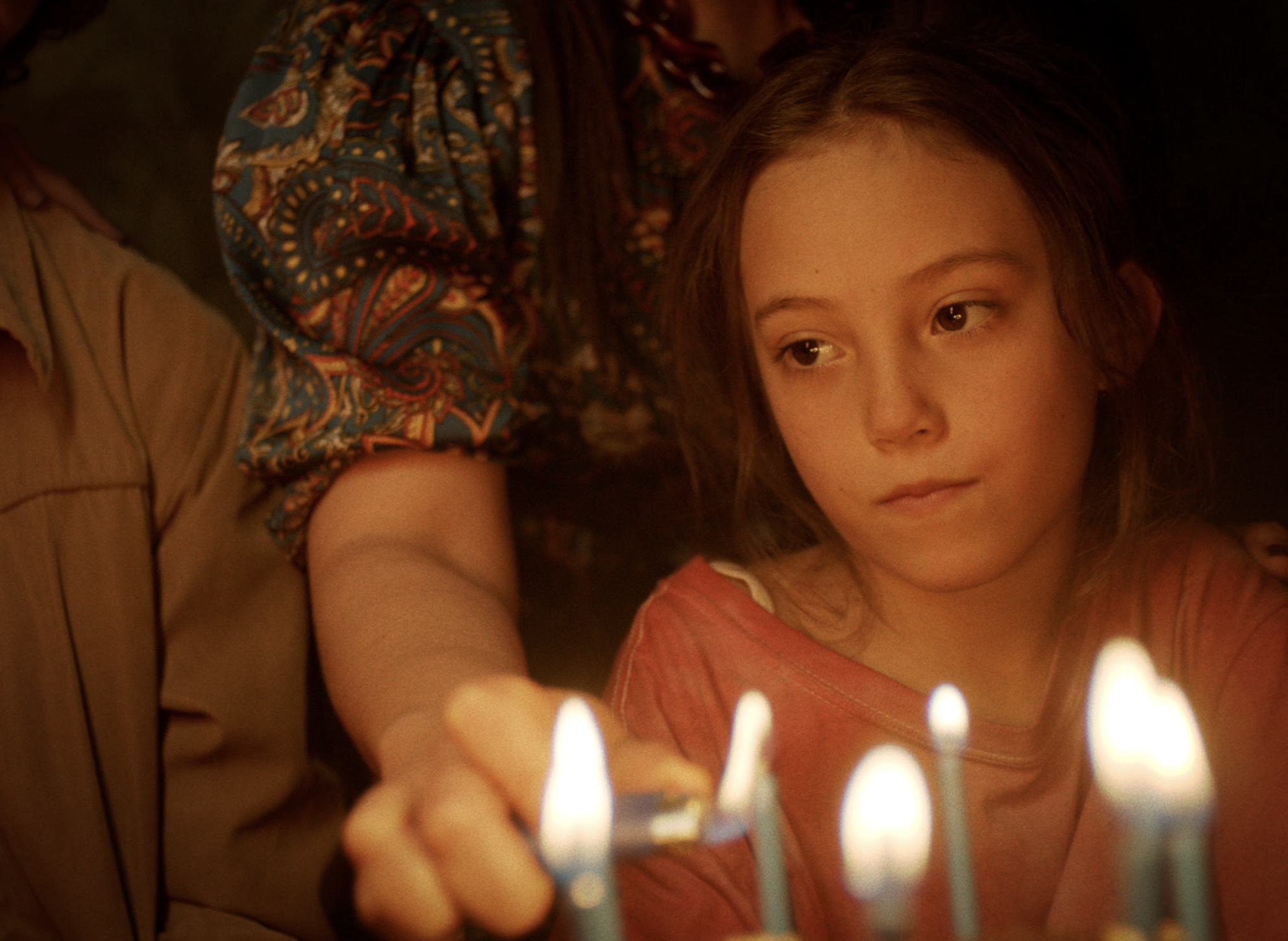 Niña mirando velas en un pastel de cumpleaños, expresión pensativa y serena, ambiente con iluminación tenue