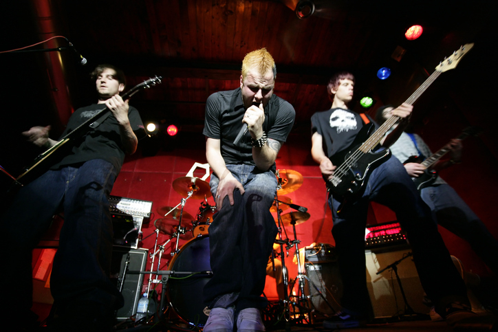 Rock band performing live; lead singer with microphone, guitarists and drummer in action