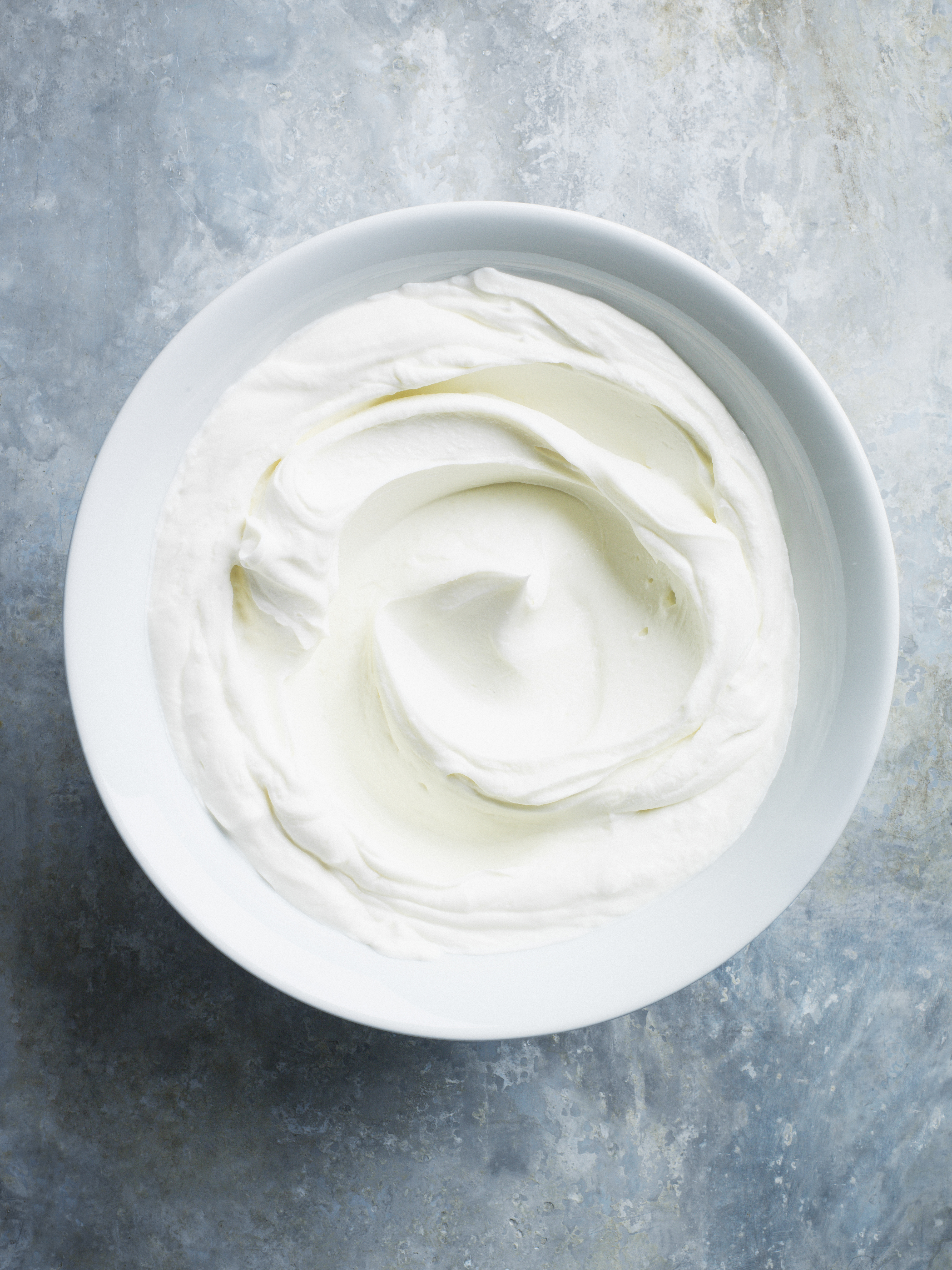 A bowl of whipped cream on a textured surface, viewed from above