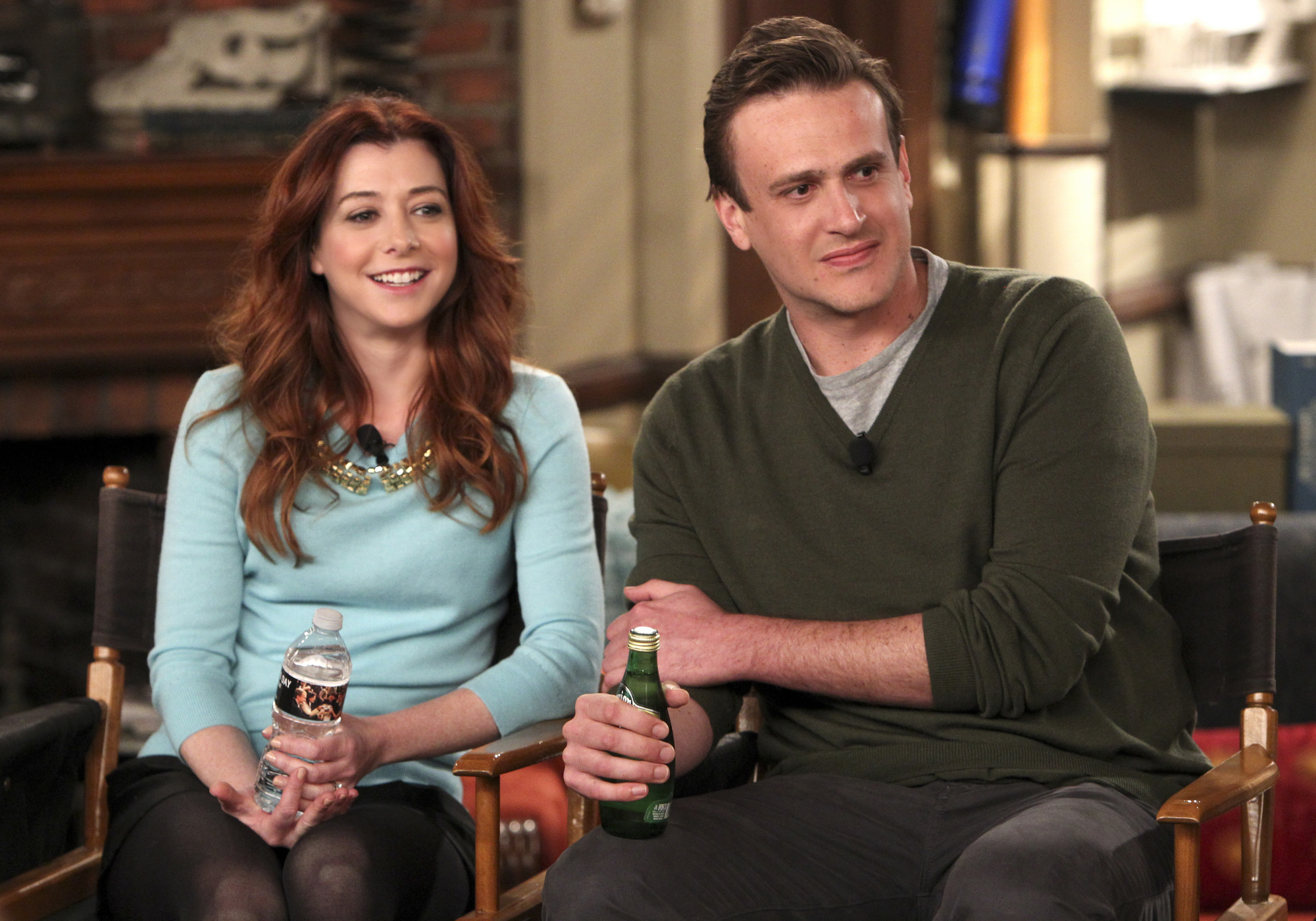 Lily and Marshall  sitting and smiling in a casual setting with water and a beer