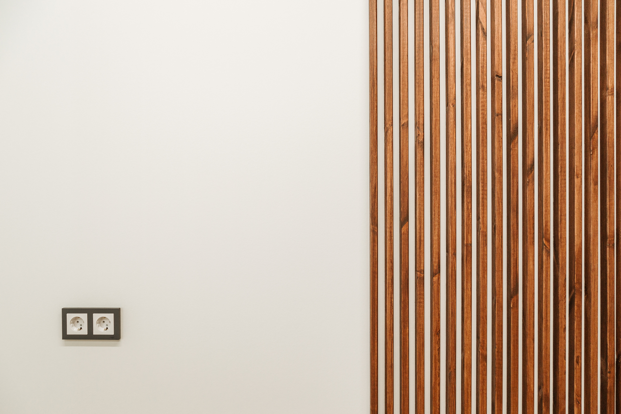 Minimalist interior with a wooden slat wall and a double electrical outlet on a plain wall