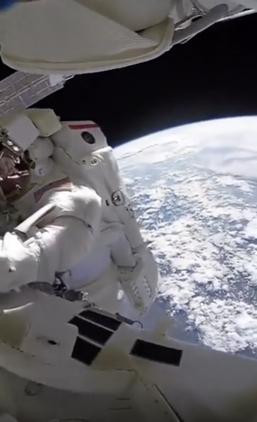 Astronaut in a white spacesuit conducts a spacewalk with a view of Earth below