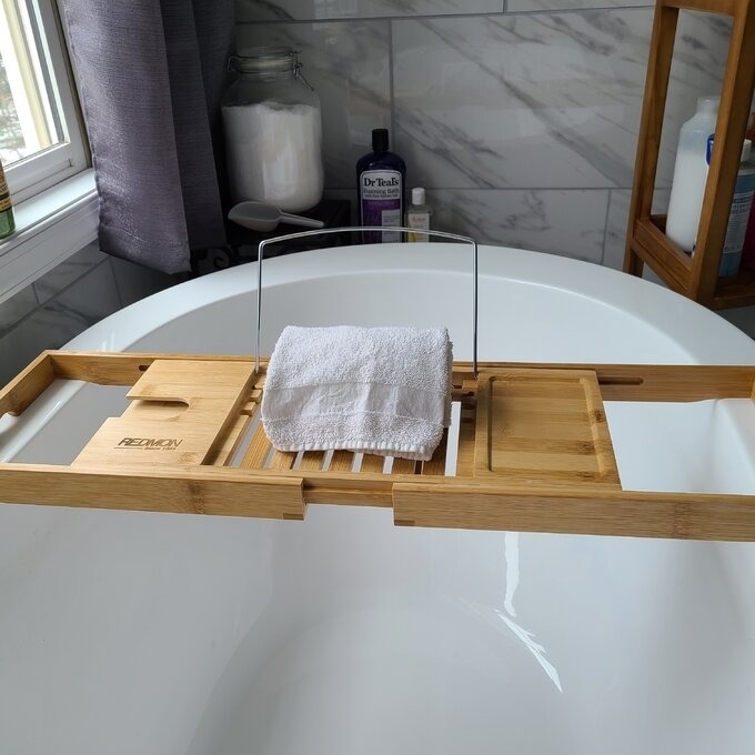 Wooden bath tray over a white tub, with a towel, in a bathroom. Perfect for a relaxing bath experience
