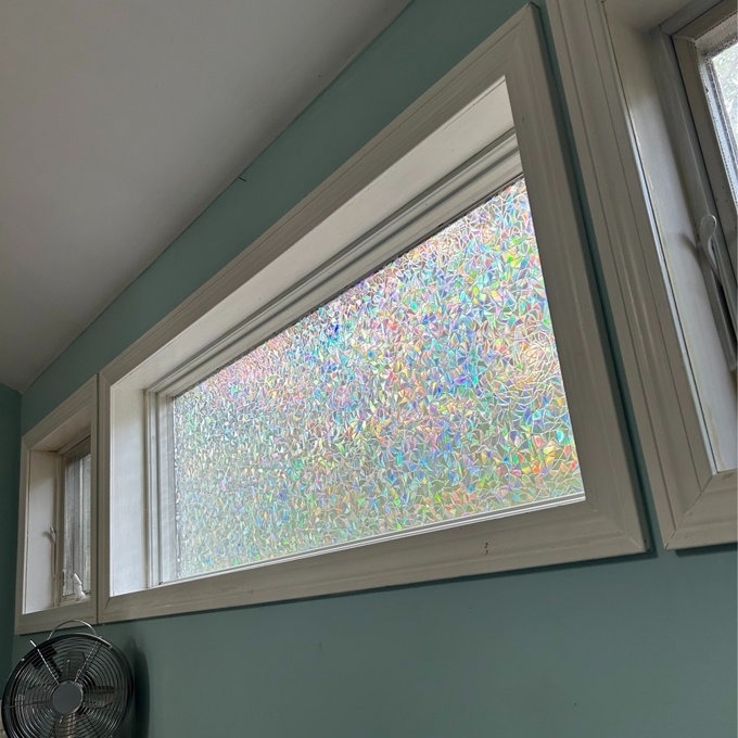 Window with privacy film casting a rainbow-like effect in a room
