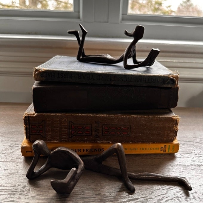 Metal bookends shaped like figures sitting on stacks of books by a window