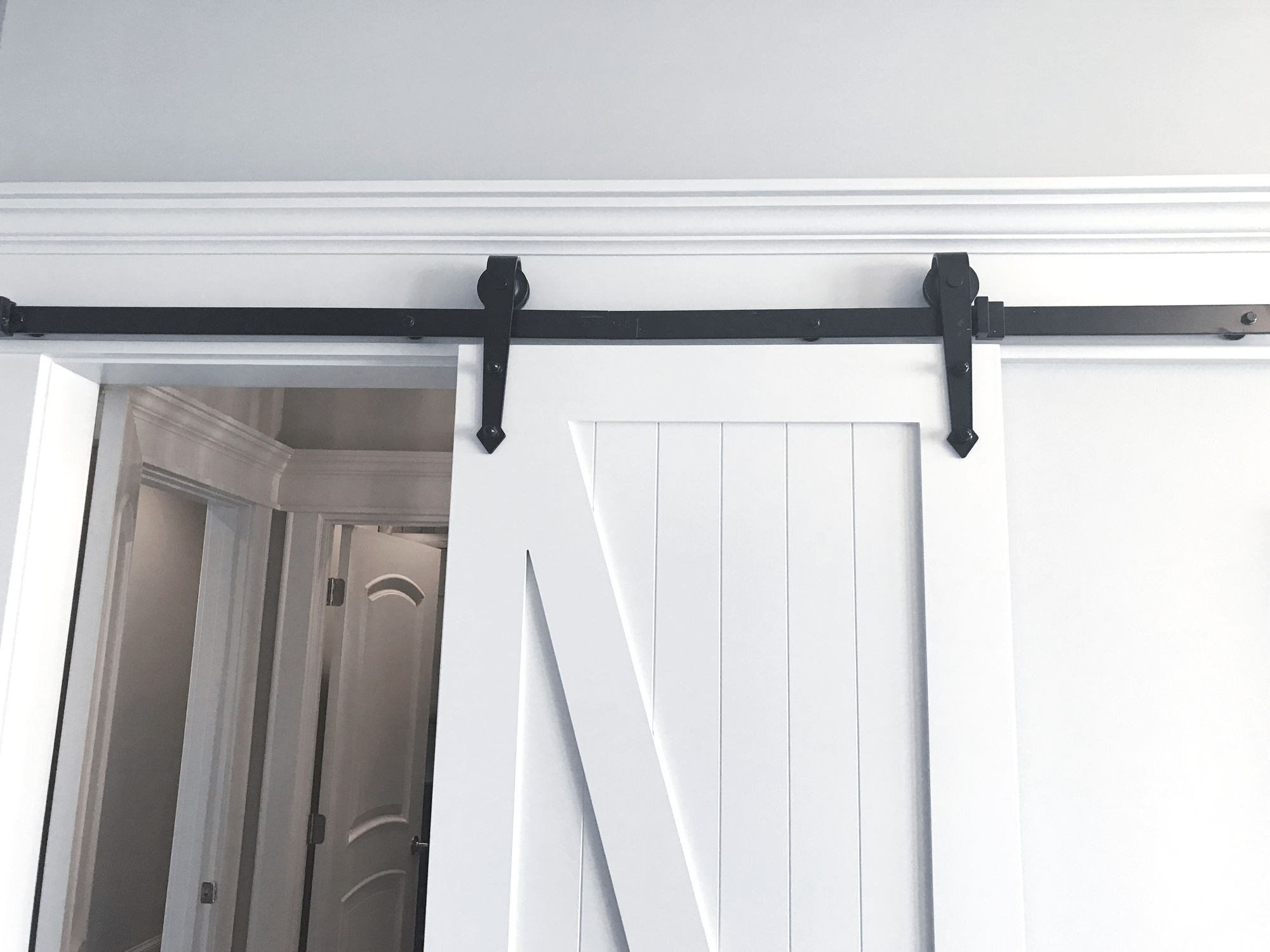 A sliding barn door with a black track system partially open, revealing an interior room