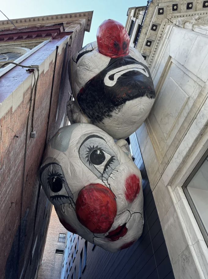 Giant puppet heads suspended between buildings, whimsical street art installation