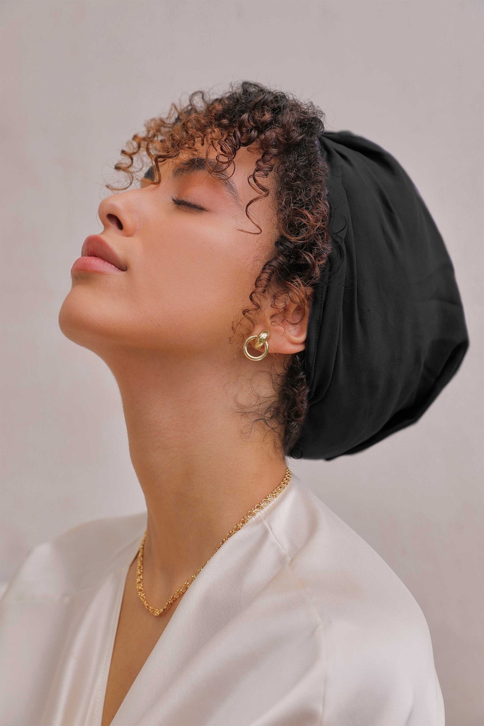 Person with curly hair wearing a silk turban and hoop earrings, eyes closed, head tilted upwards