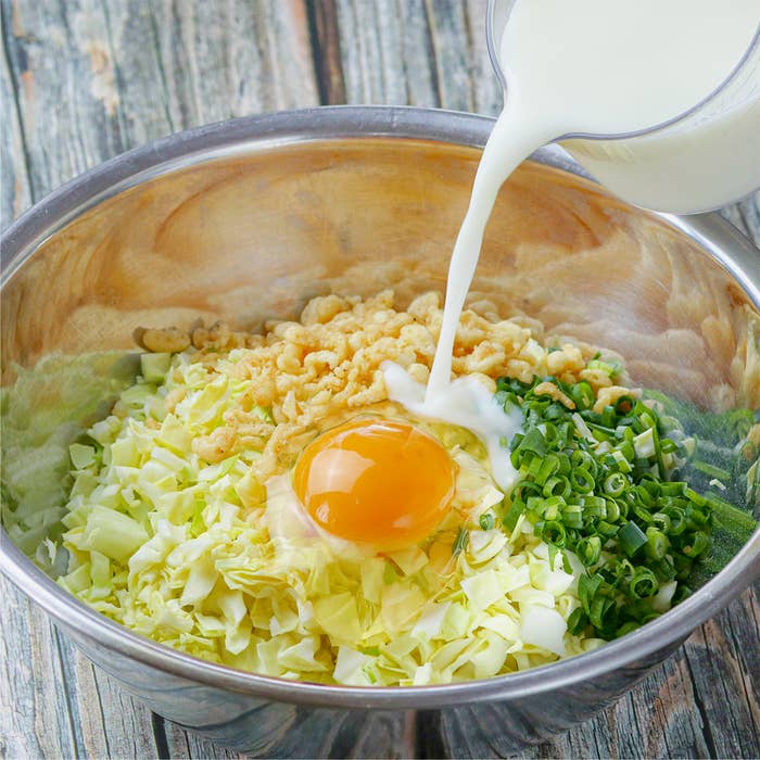 ボウルにキャベツ、ネギ、卵、牛乳が入っている料理の下ごしらえ。